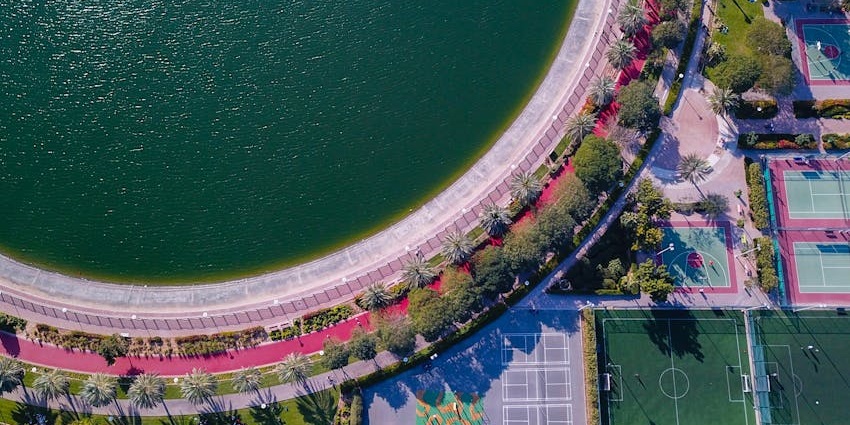 Aerial view of Al Barsha Pond Park in Dubai with pond, jogging tracks, and sports courts.
