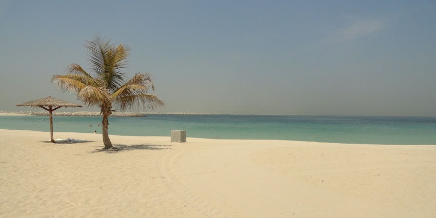 Sandy beach at Al Mamzar Park in Dubai with a tree and a shaded structure, one of the parks in Dubai.