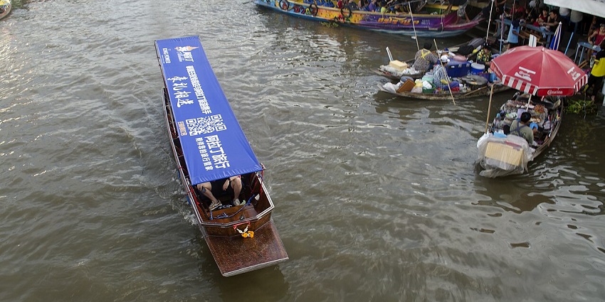 A large crowd of boats on a river, with some docked along the shore where vendors are.
