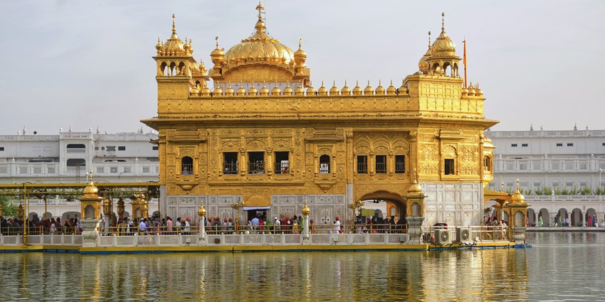 Golden Temple in Amritsar shines under daylight, reflected in the surrounding water with devotees.