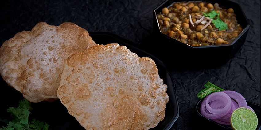 A black plate holds two pieces of poori, with a bowl of chickpea curry nearby, one of the best Indian restaurants in Singapore, Little India.
