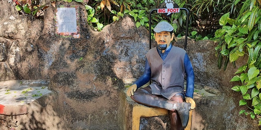 Colourful statue of a seated man at Big Foot Museum in Goa, surrounded by greenery.