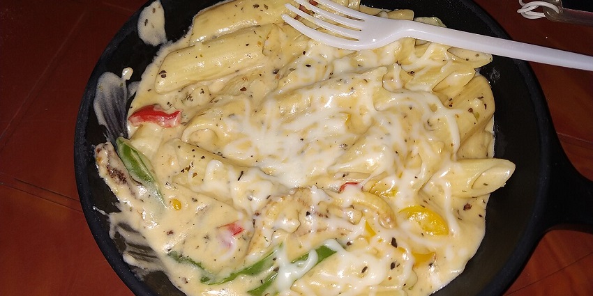 A plate of creamy white sauce pasta with a plastic fork is served at one of the vegetarian restaurants in Havelock Island.