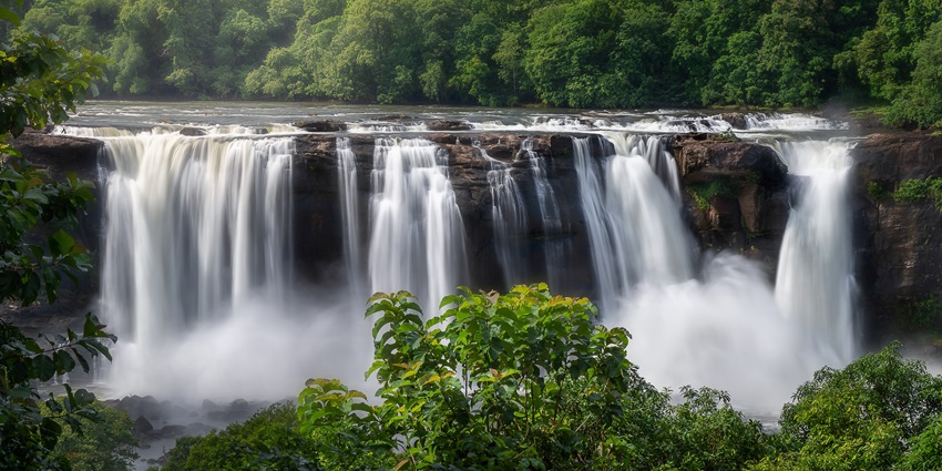 Wide view of Athirappilly Waterfalls surrounded by lush green forest landscape.