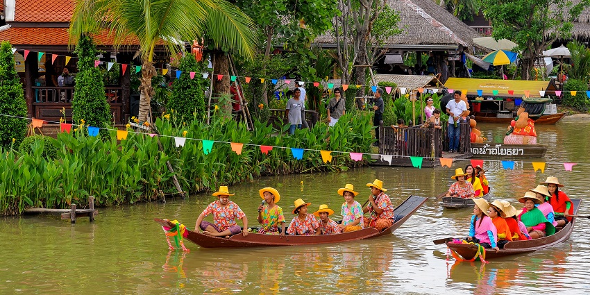 Boats with people floating peacefully at Ayothaya Floating Market in Thailand.
