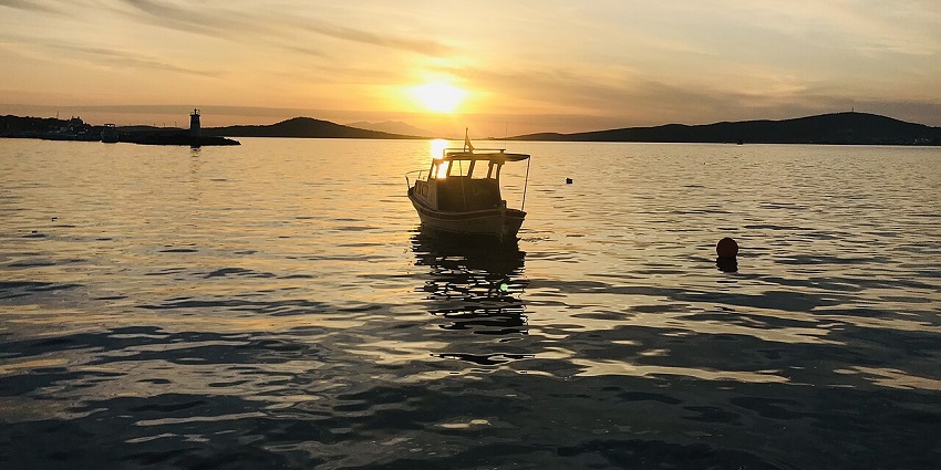 A fishing boat on calm waters at sunset with golden horizon, a scenic spot for scuba diving in Turkey.
