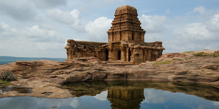 Ancient Northern Fort Temple in Badami with reflection in water under a cloudy sky.