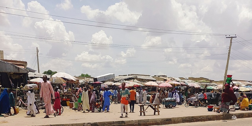 A wide-angle view of a bustling outdoor market with many people, stalls, and umbrellas.