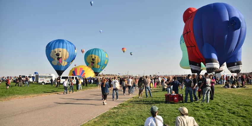 Unique hot air balloons at Albuquerque International Balloon Fiesta with people sitting, walking, and watching launches.