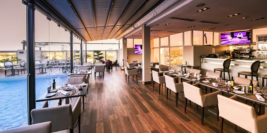 A large, modern, empty restaurant with a wooden floor and a rooftop pool next to it, one of the South Indian Restaurants in Singapore.

