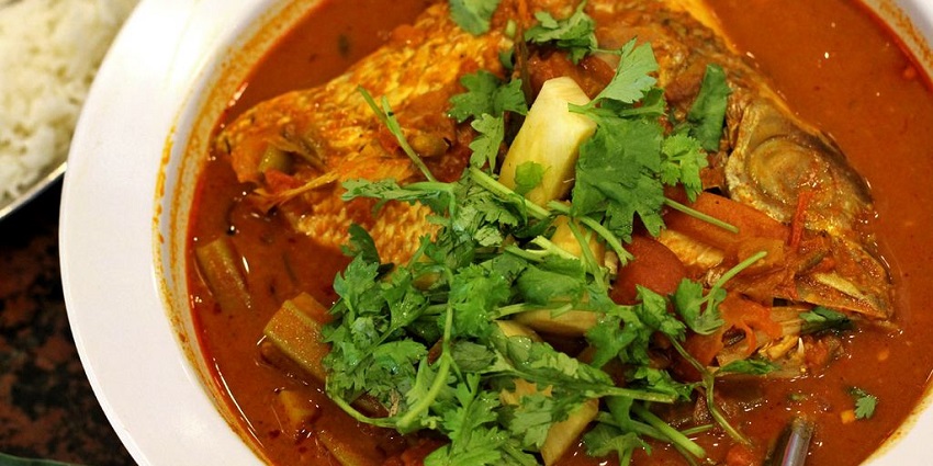 A top-down view of a large bowl of fish curry with a whole fish and vegetables with coriander in one of the best Indian restaurants in Singapore, Little India.
