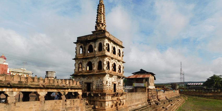 A multi-level stone structure with a tall spire stands next to a low wall and stone stairs.