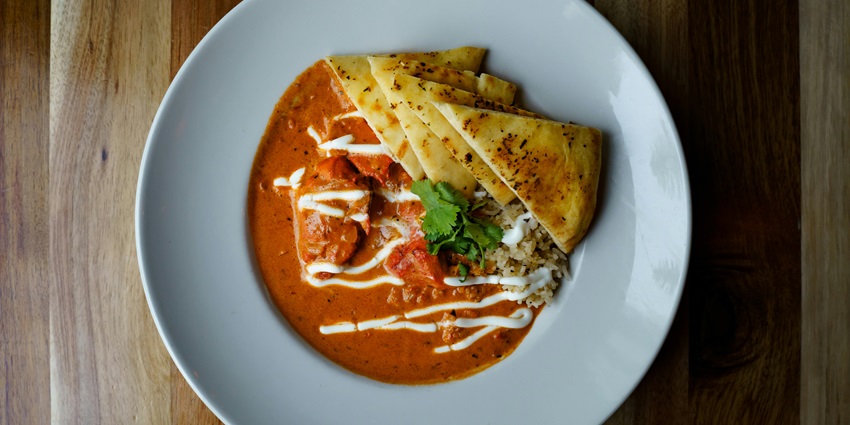 Butter chicken served with a side of flatbread on a plate.