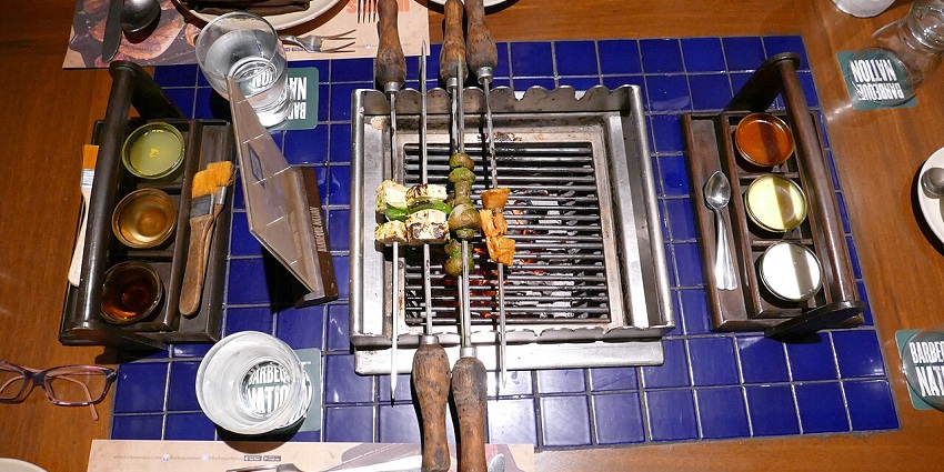 A close-up view of several metallic skewers laden with food items, waiting to be grilled.
