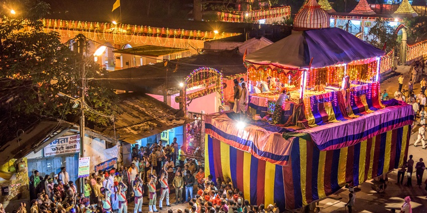 People gathered in a small area, watching a huge chariot being carried by people on Dussehra.