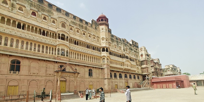 A grand fort with red sandstone walls, towers, and bastions stands on a flat plain surface.