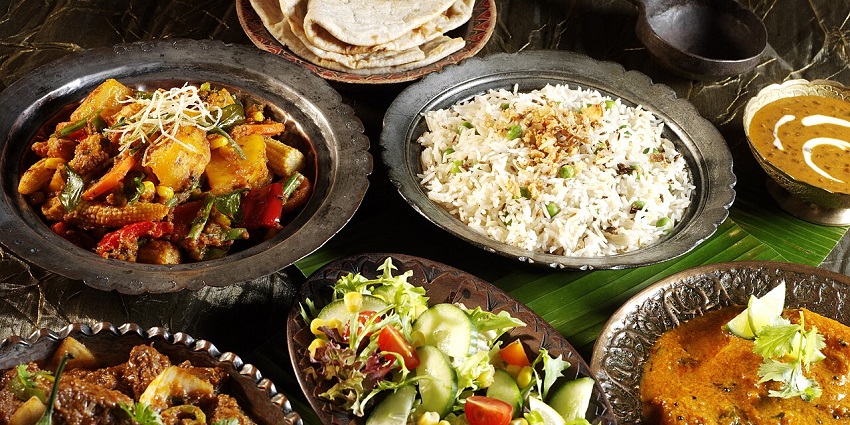Indian meal with curries, rice, flatbread, and salad served in traditional metal bowls.