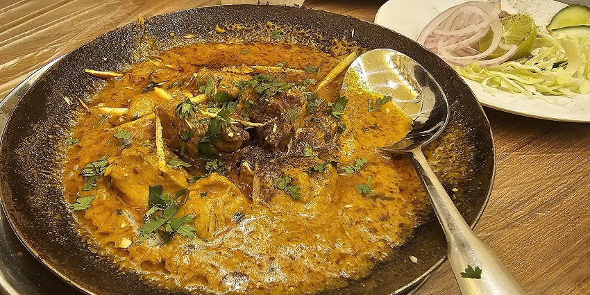 A pan of rich, flavourful Indian lamb curry garnished with fresh cilantro and ginger.
