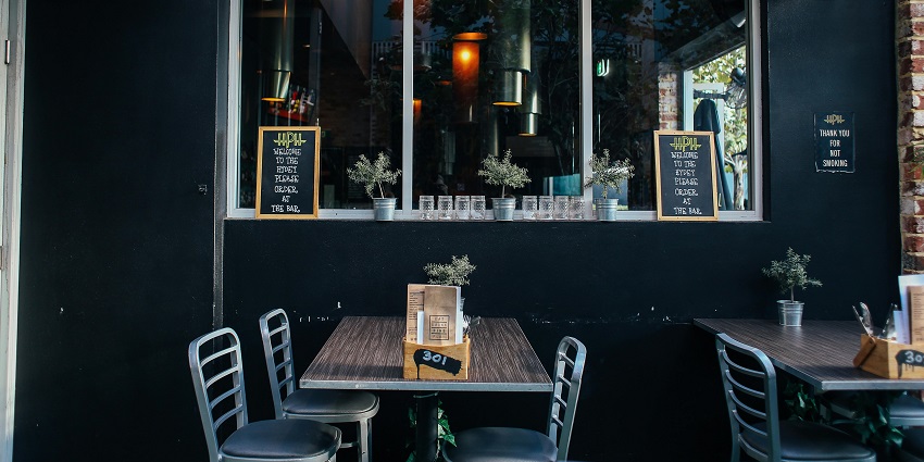 Small restaurant patio featuring simple seating, dark walls, and potted plants for décor
