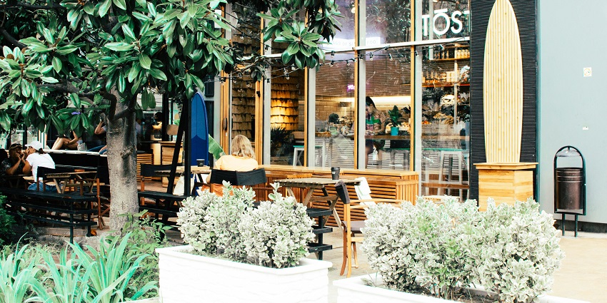 Outdoor seating at Cafe Chhappan Bhog with a black and brown wooden dining set, plants, and daytime ambiance.
