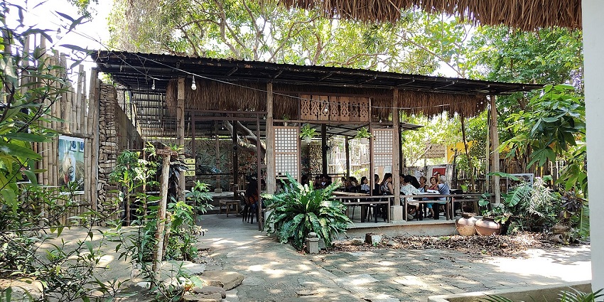 Open-air café with bamboo walls, thatched roof, and lush greenery creating a rustic vibe, one of the best cafes in Kalimpong.
