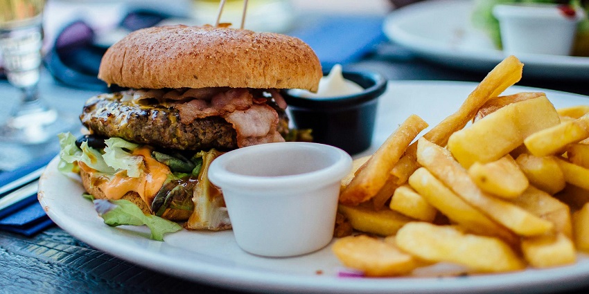 Juicy burger with bacon, lettuce, and fries served on a plate with dipping sauce.