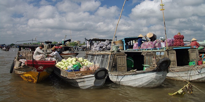 Wooden boats tied together, filled with vendors and their goods, at a floating market.
