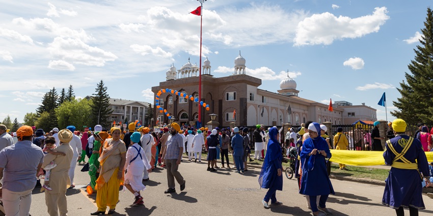 Sikh devotees in colourful attire gather and walk outside a Gurdwara during Nagar Kirtan parade.