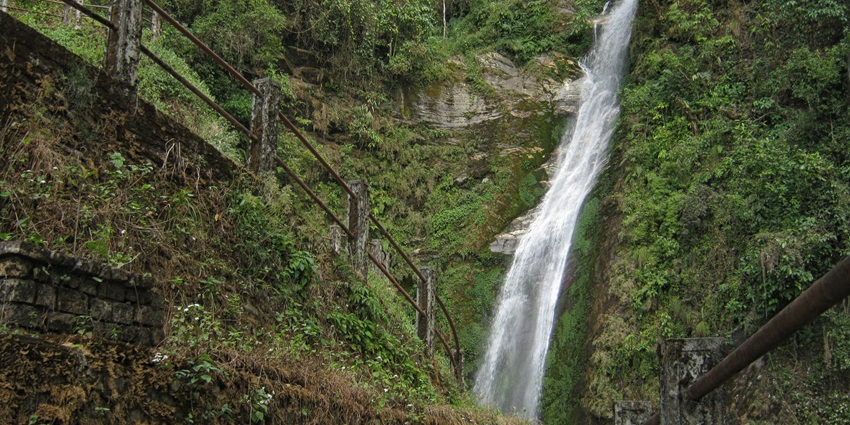 Tall waterfall flowing down a cliff surrounded by dense greenery at Changi, Darjeeling.