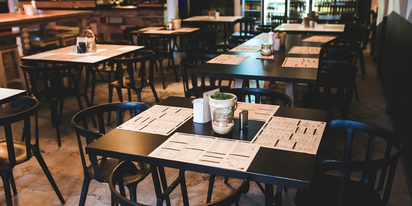 Empty restaurant dining area with black tables, menus laid out, and a bar in the background, one of the best restaurants in Orchard.