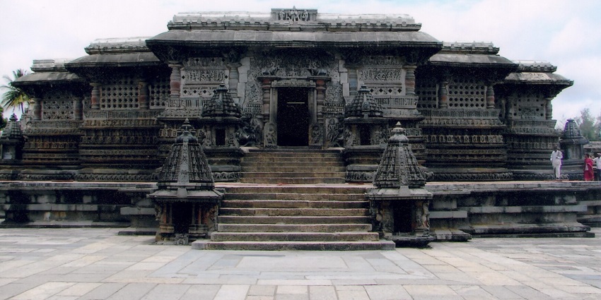 A symmetrical stone temple with intricate carvings and multiple levels sits under a partly cloudy sky.