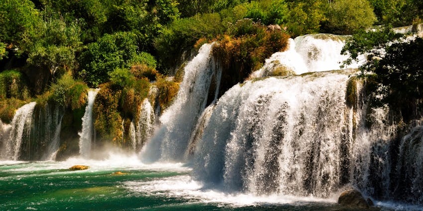 Seasonal waterfalls flowing over rocks, surrounded by dense forest at Chidiya Tapu.
