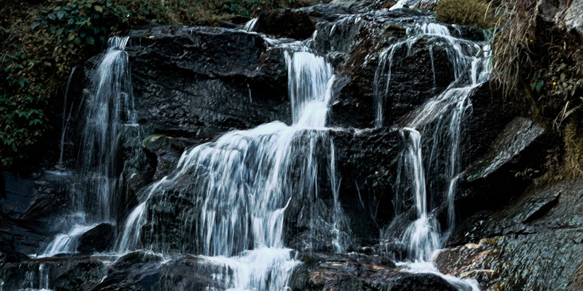 Waterfall cascading down rocky cliffs surrounded by greenery and misty mountain views.