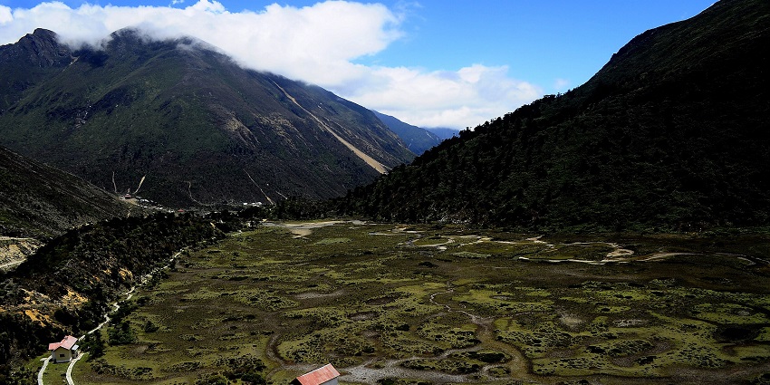 Chopta Valley from above with a few buildings surrounded by greenery and dark mountains.
