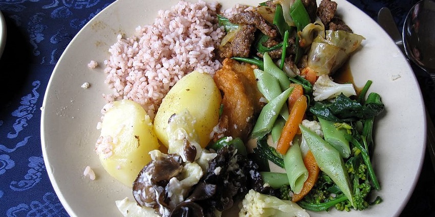 The food served in bowls includes potatoes, Bhutanese red rice, greens, and mushrooms, one of the Indian restaurants in Bhutan.
