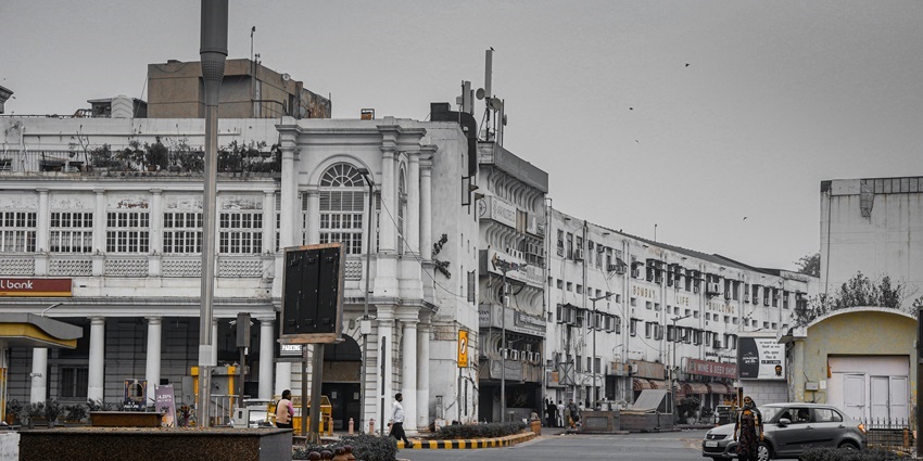 Streets of Connaught Place in Delhi with shops and vehicles during the day.