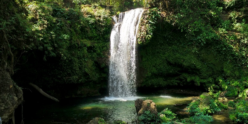 Corbett Waterfall cascading from a rocky cliff surrounded by lush green forest and a pool.