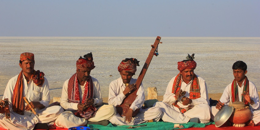Folk musicians in traditional attire performing at Rann Utsav with instruments and vibrant turbans.