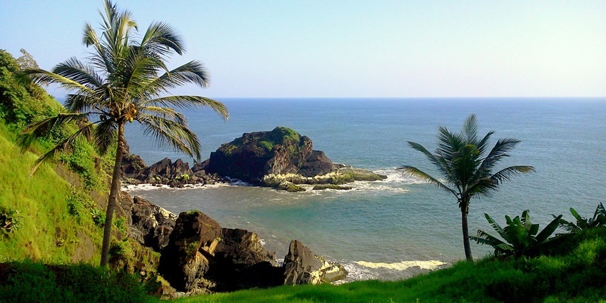 Coastal view in Cumbarjua Goa, with sandy shoreline, blue water, and green hills.