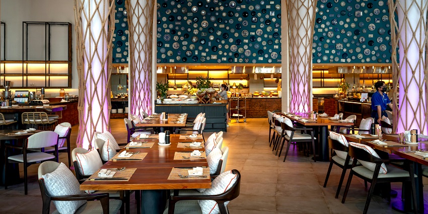 Vibrant restaurant with tall rope-wrapped pillars, blue plate wall art, and an open kitchen among the multiple restaurants in Havelock Island.
