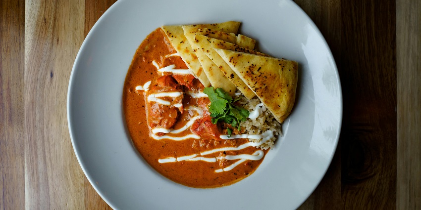 Close-up of chicken curry with a slice of flatbread served on a restaurant plate.
