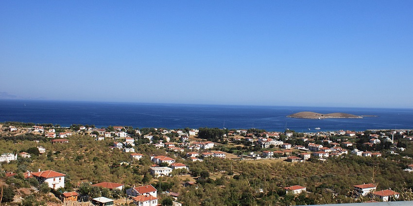 An elevated view of a coastal town with red roofs, blue sea, and an island, ideal for scuba diving in Turkey.
