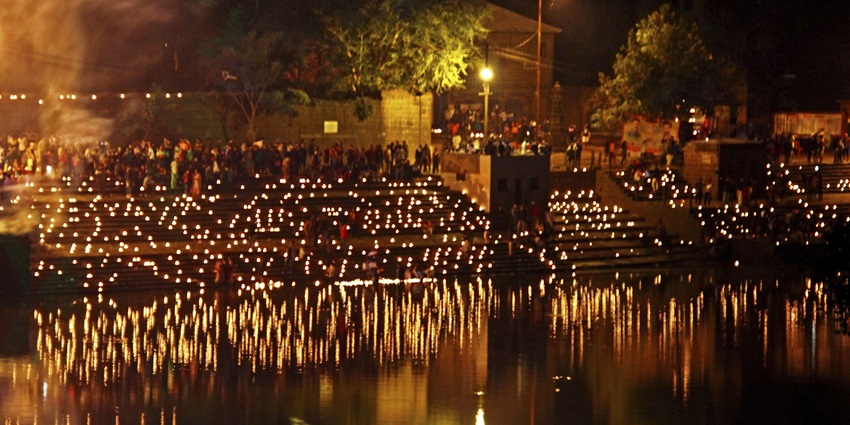 Soft glow of thousands of lit candles on a riverside as people gather in quiet light.