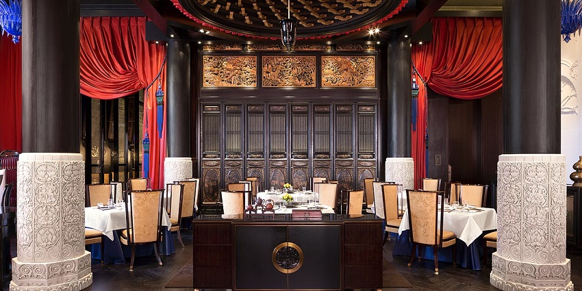 A formal dining room with red curtains, white tablecloths, and ornate wall carvings.
