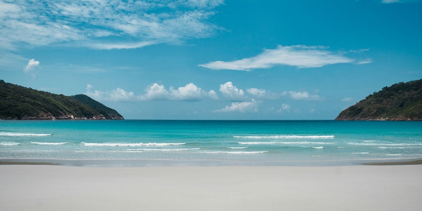 A serene stretch of golden sand at Devbagh Beach with calm blue sea and clear sky.
