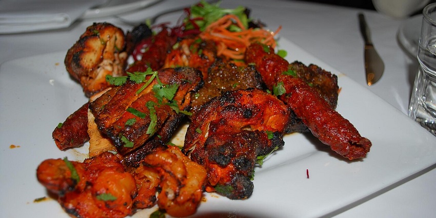 A plate of flavoured tandoori meats, chicken, and kebabs, garnished with some fresh cilantro.
