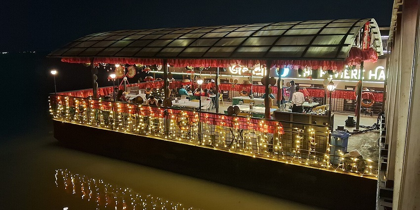 A floating restaurant lit up, warm orange and yellow lights reflecting gently on the water.