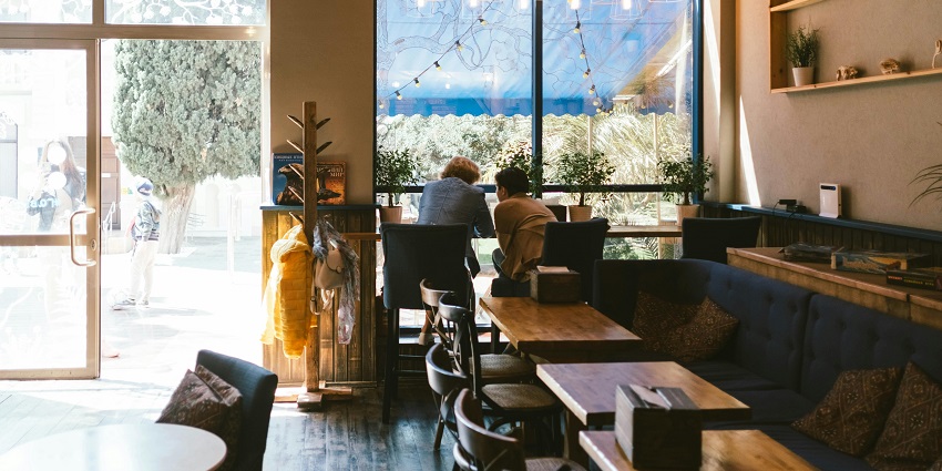 Cosy café interior with wooden tables, hanging lights, and two people seated by the window.