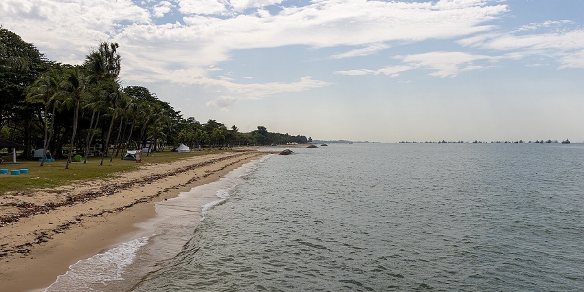 Beach at East Coast Park in Singapore with sandy shore and lush trees nearby.
