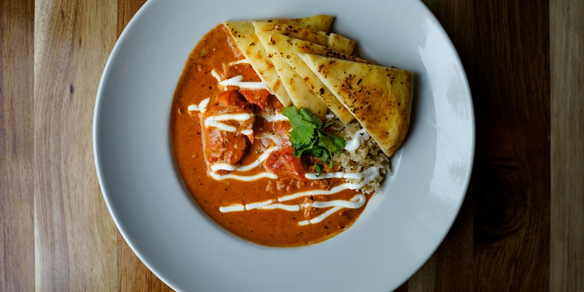 Butter chicken with flatbread served on a plate at a rooftop restaurant setting.
